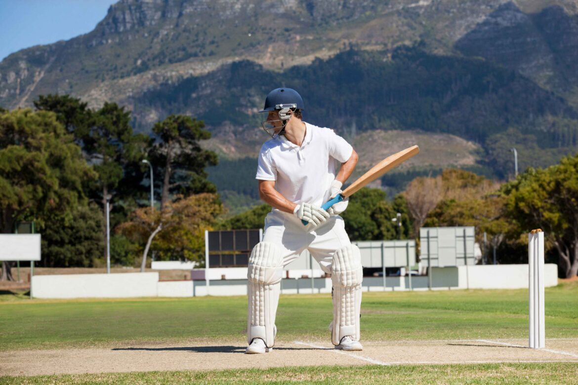 Batsman playing cricket on field against mountain during sunny day in test match clothes, representing the concept of highest batting average in test cricket history