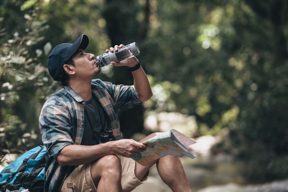 Young hiker taking a break for drinking water to stay hydrated during hiking