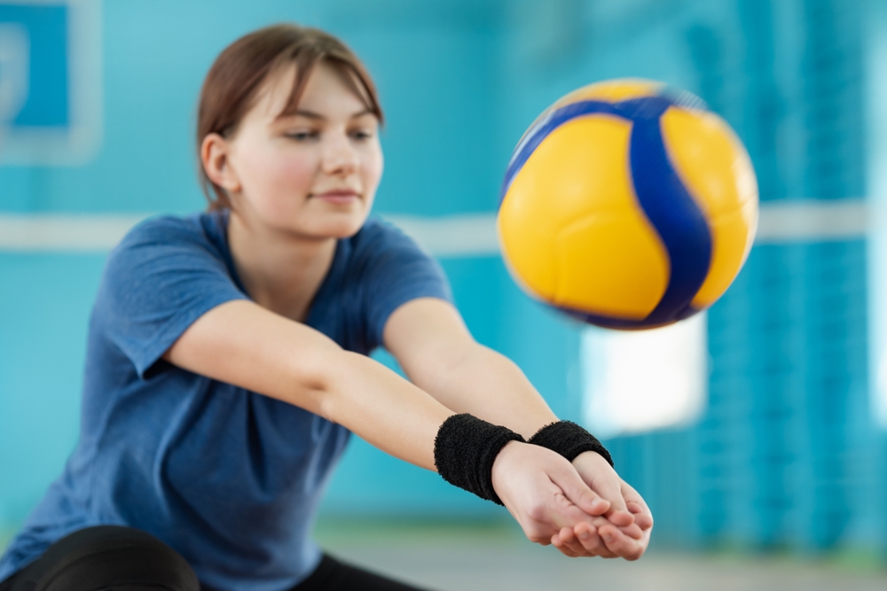 Practicing digging skills during volleyball training on court. Young girl practicing fundamental volleyball skills, physical education concept