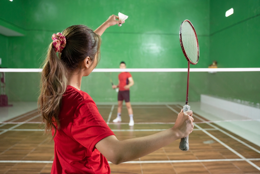 Female badminton player holding shuttlecock and racket with good grip in service position