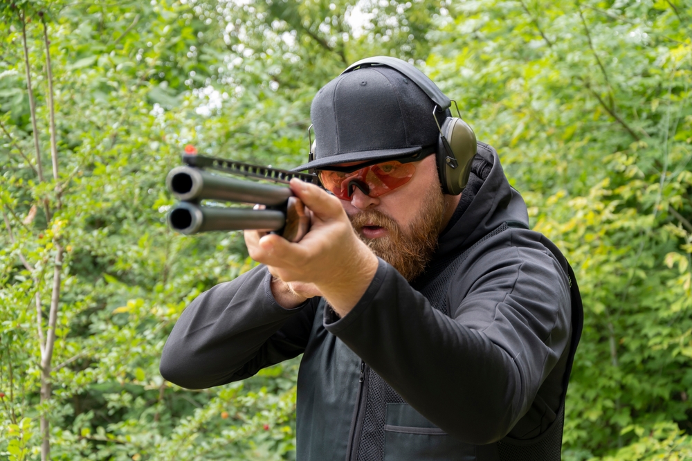 A calm and mentally strong male shooter aims a sporting double-barreled hunting rifle, target shooting, bench shooting.