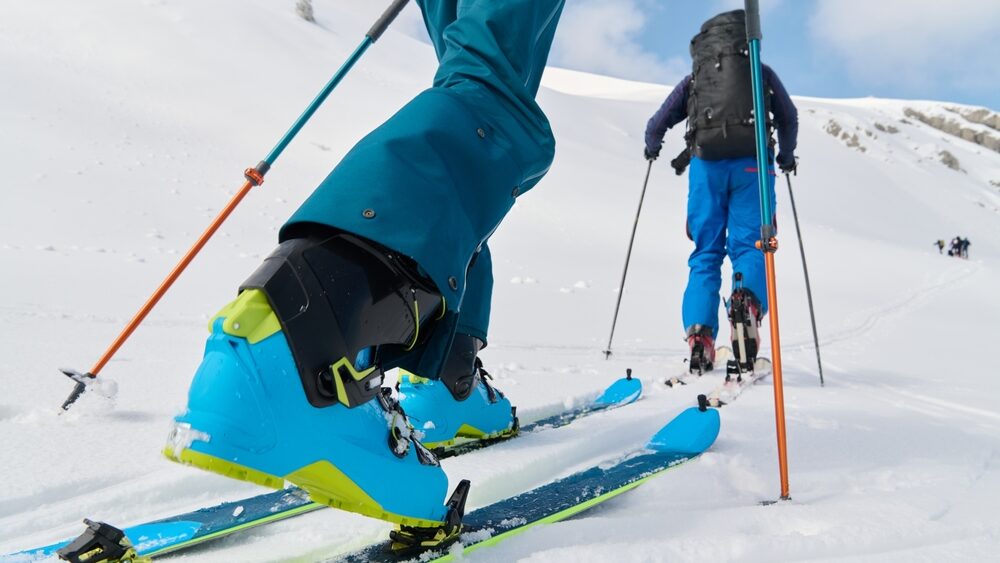 close up of skiing boot while the person skiing behind another person on mountain covered with snow